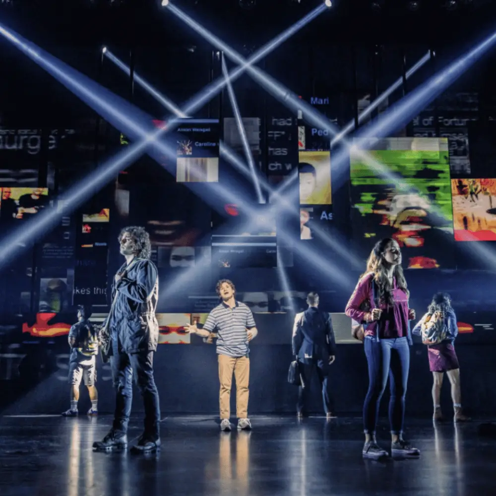 Performers on a Broadway stage lit by crossing beams of stage lighting